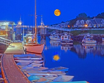 May include: A night scene with a full moon over a harbor with several boats docked. The boats are mostly white with blue accents. There are several smaller boats docked in the foreground.