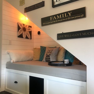 Puede incluir: Una cama blanca integrada con un colchón gris y tres cajones. La cama está debajo de una escalera con paredes blancas y una variedad de letreros enmarcados con citas inspiradoras. Los letreros incluyen "Live Well Love Much", "Family", "Happy is What We Make It", "Love All Of You", y "Bindle est. 11.8.98".