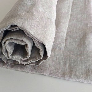 May include: A rolled up light gray linen throw blanket with a quilted pattern. The blanket is folded in half and rolled up, with the seam visible.