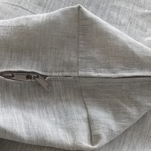 May include: A close-up of a gray zipper sewn into a gray fabric pillow cover.