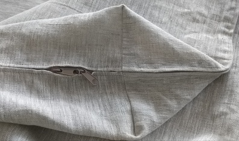 Puede incluir: Primer plano de una cremallera gris cosida en una funda de almohada de tela gris.