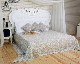 May include: A white bed with a white headboard and a beige patterned bedspread. The bed is made with white pillows and a white blanket. There is a tray with pastries on the bed.