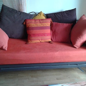 Puede incluir: Un div&aacute;n de metal negro con un colch&oacute;n de lino rojo y varios cojines de colores vivos. Los cojines son en tonos de rojo, naranja, marr&oacute;n y amarillo.