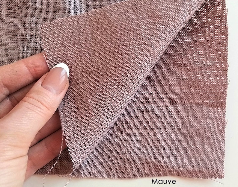 Puede incluir: Un primer plano de una tela de lino de color malva. La tela tiene un tejido texturizado y est&aacute; doblada por la mitad. La palabra "Malva" est&aacute; impresa en blanco en la parte inferior de la imagen.