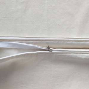 Op de afbeelding: Een witte kussensloop met rits en een rits-schuif in het midden.