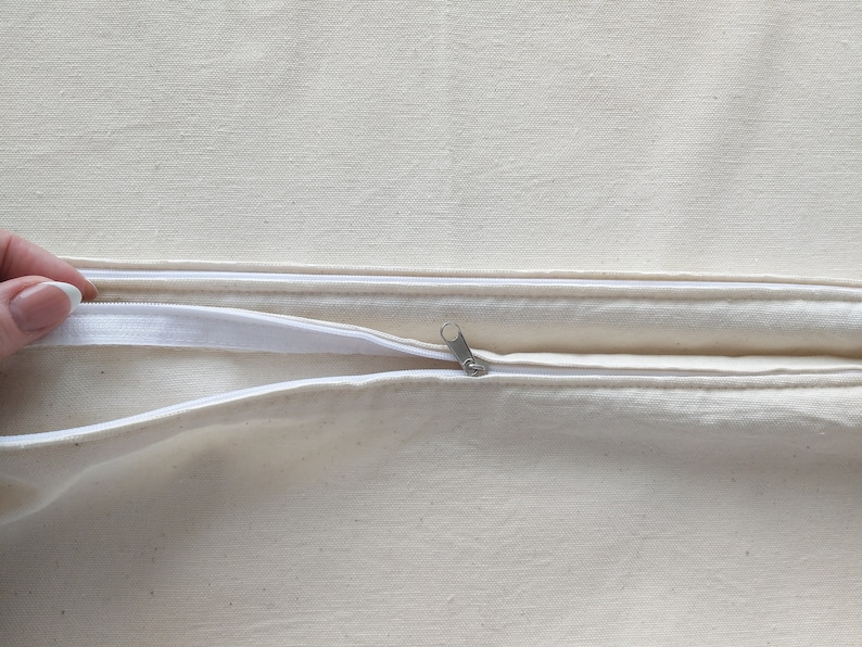 Op de afbeelding: Een witte kussensloop met rits en een rits-schuif in het midden.