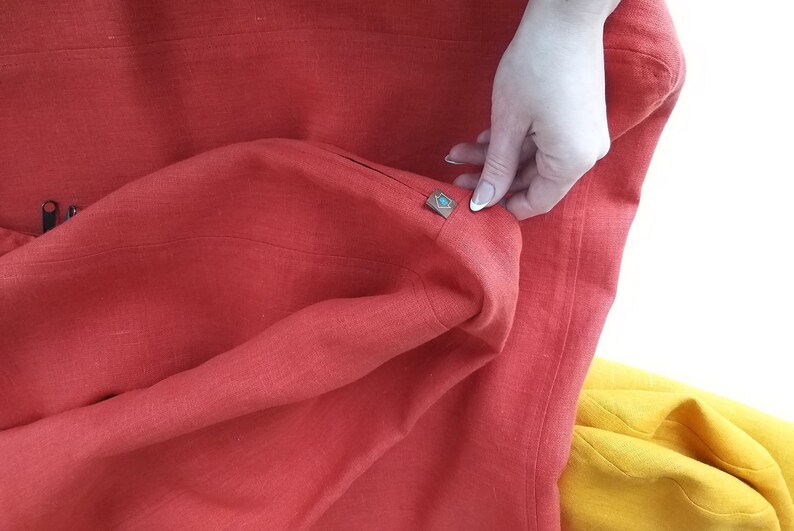 Puede incluir: Una tela de lino roja con una peque&ntilde;a etiqueta azul y dorada cosida en la esquina.