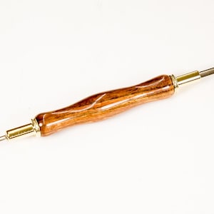May include: A seam ripper with a wooden handle and metal blades. The handle is a warm brown color with a curved design. The metal components are silver and gold. A small red bead is visible on each blade tip.