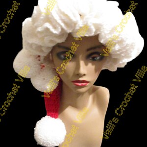 May include: White crocheted Santa hat with a red pom-pom and a white pom-pom on the top. The hat is on a mannequin head.