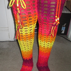 May include: A pair of handmade, open-weave crochet knee-high socks. The socks feature a vibrant gradient of colors, transitioning from yellow to orange, then to pink and purple. Decorative tassels and beads adorn the top.