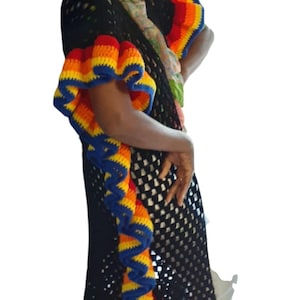 Può includere: Abito nero all'uncinetto con finiture e maniche arcobaleno. L'abito presenta un vivace motivo rosso, arancione, giallo e blu. Il testo "Valli's Crochet Boutique" è visibile nella parte inferiore dell'abito.