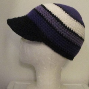 Pode incluir: Um chapéu de crochê listrado em roxo, branco e preto com uma aba preta.