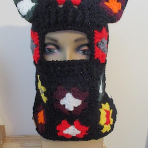 May include: Black crochet balaclava with colorful square designs and cat ears. The balaclava has a hole for the eyes and mouth. "Valli's Crochet Boutique" is written on the bottom of the image.