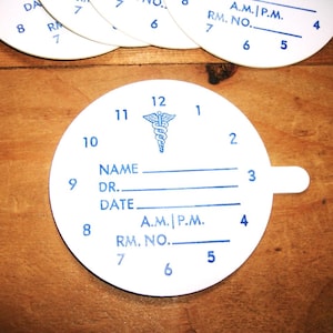 May include: White, circular medical chart with blue text and a caduceus symbol. The chart includes spaces for name, doctor, date, and room number, with A.M./P.M. indicators. Additional charts are visible in the background.