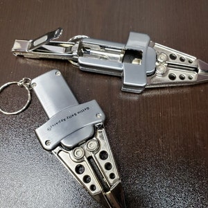 May include: Two silver multi-tool keychains. The keychain on the left has the text "Safety Apparel" on the side. The keychain on the right has a nail clipper.