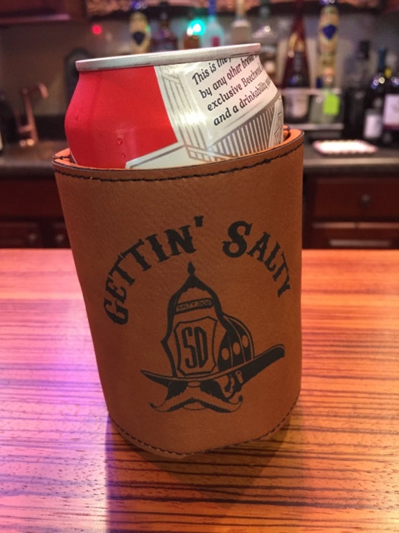 May include: Brown leather can cooler with the text "GETTIN' SALTY" and a black and white illustration of a firefighter's helmet with a moustache.