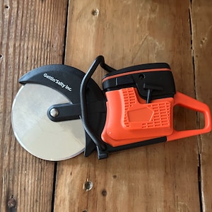 May include: A black and orange pizza cutter with a round blade and a handle with a lever. The blade has the text "Gettin' Salty inc" printed on it.