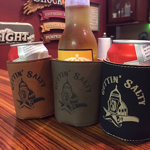May include: Three brown leather can coolers with the text "Gettin' Salty" and a firefighter helmet logo. The coolers are holding a beer bottle and two cans.