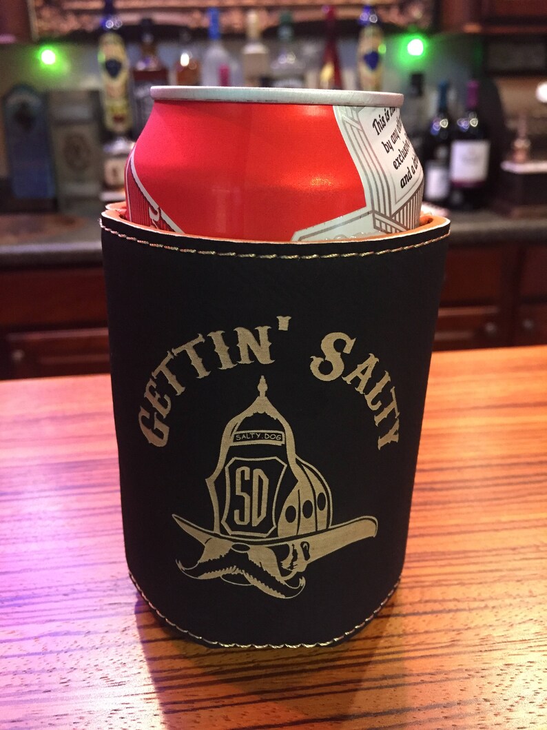May include: Black neoprene can cooler with a gold stitched border and the text "Gettin' Salty" in gold lettering. A gold firefighter helmet with a moustache and the text "Salty Dog" is in the centre of the cooler.