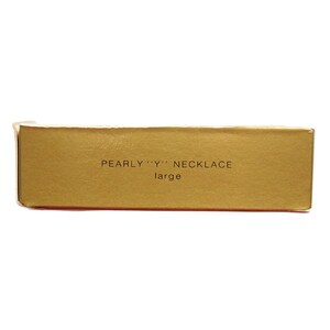 Peut inclure: Une bo&icirc;te dor&eacute;e avec le texte "PEARLY "Y" NECKLACE large" imprim&eacute; dessus.