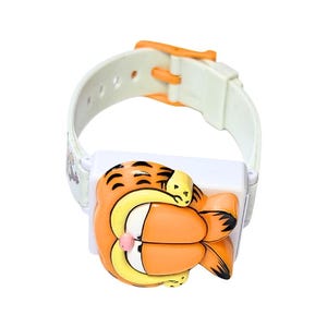 May include: A white and orange Garfield watch with a cartoon Garfield character design. The watch has a white strap with an orange buckle. The watch face features a 3D Garfield character in orange, yellow, and black.