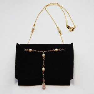 Peut inclure: Un collier en cha&icirc;ne dor&eacute;e avec des accents de perles blanches. Le collier a un pendentif &agrave; goutte avec une seule perle &agrave; l'extr&eacute;mit&eacute;. Le collier est pr&eacute;sent&eacute; sur un fond de velours noir.
