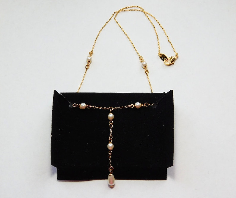 Peut inclure: Un collier en cha&icirc;ne dor&eacute;e avec des accents de perles blanches. Le collier a un pendentif &agrave; goutte avec une seule perle &agrave; l'extr&eacute;mit&eacute;. Le collier est pr&eacute;sent&eacute; sur un fond de velours noir.