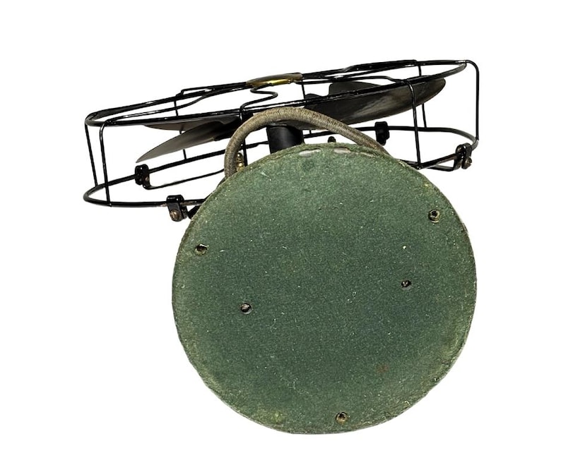 May include: An antique electric fan with a black metal cage and blades. The base is a circular shape covered in green felt. The fan's design is vintage, with a focus on functionality and a classic aesthetic.