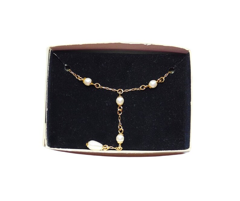 Peut inclure: Un collier en cha&icirc;ne dor&eacute;e avec cinq accents de perles blanches. Le collier est pr&eacute;sent&eacute; dans un coffret en velours noir.