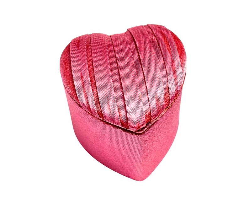 May include: A pink heart-shaped jewelry box with a satin ribbon design.