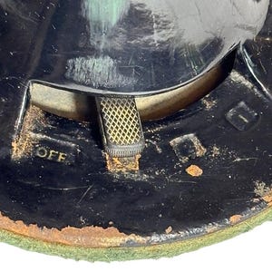 May include: Close-up of a vintage black object with a gold-colored switch and the word "OFF" in gold lettering. The object has a circular shape with a green felt base and signs of wear and tear.