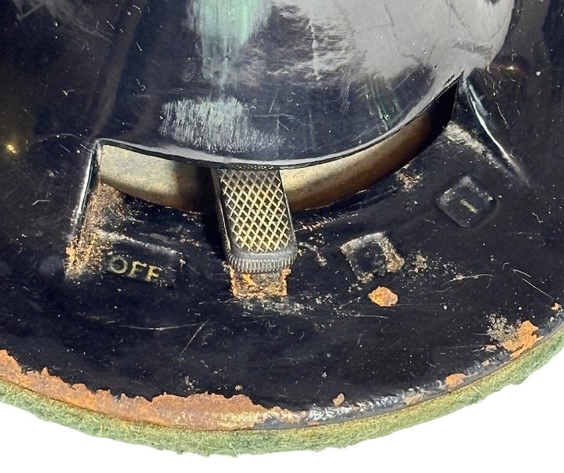 May include: Close-up of a vintage black object with a gold-colored switch and the word "OFF" in gold lettering. The object has a circular shape with a green felt base and signs of wear and tear.