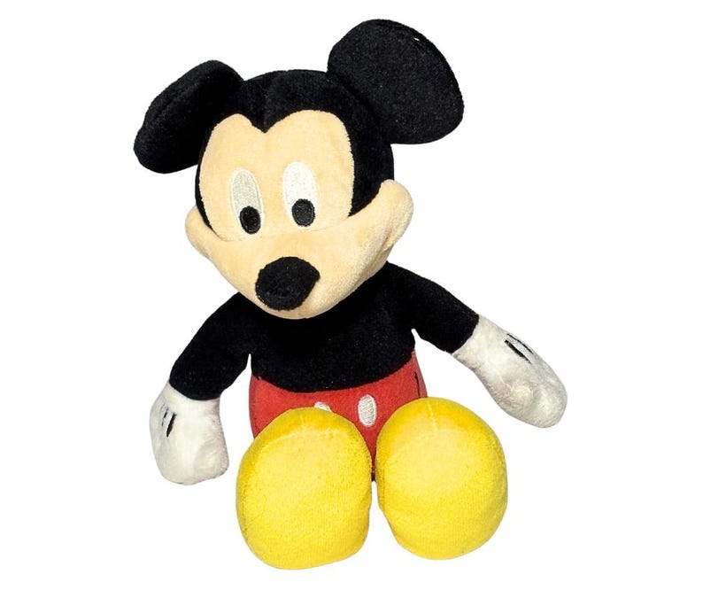 May include: A plush Mickey Mouse toy, featuring black ears, a black body, and a cream-colored face. The toy has red shorts, yellow feet, and white gloves. The iconic Disney character is sitting.