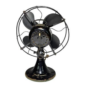May include: An antique black electric fan with four blades, a protective cage, and a round base. The fan has a vintage design with a glossy finish and visible wear, suggesting its age and use. The fan is a classic example of early 20th-century home appliances.
