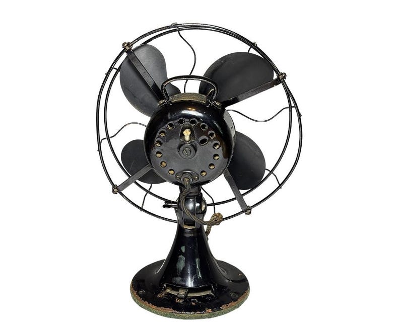 May include: An antique black electric fan with four blades, a protective cage, and a round base. The fan has a vintage design with a glossy finish and visible wear, suggesting its age and use. The fan is a classic example of early 20th-century home appliances.