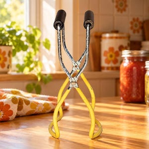 Vintage jaren 70 zwarte weckpottang met houten handvat en gele rubberen grepen.