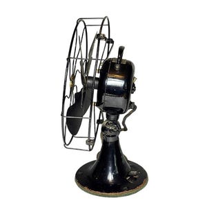 May include: Vintage black electric fan with a circular wire cage and a black base. The fan has a curved blade and a handle on top. The base is round and has a green trim. The fan is a classic design.