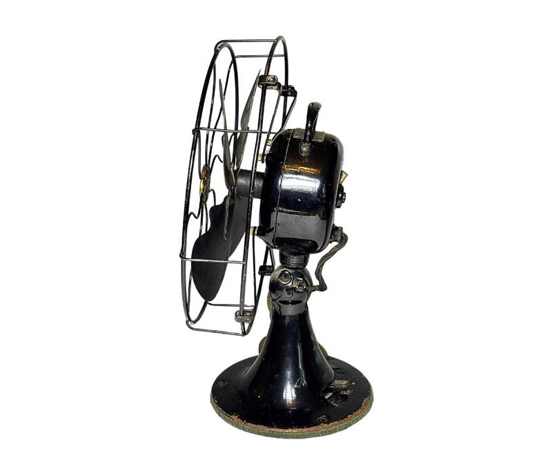 May include: Vintage black electric fan with a circular wire cage and a black base. The fan has a curved blade and a handle on top. The base is round and has a green trim. The fan is a classic design.