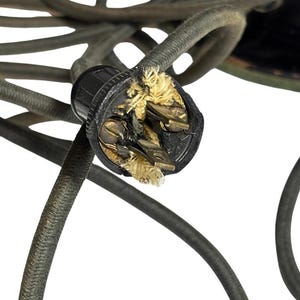 May include: Close-up of a damaged black electrical plug with exposed wires and frayed insulation. The plug is surrounded by several dark gray, braided electrical cords, suggesting a potential electrical hazard.