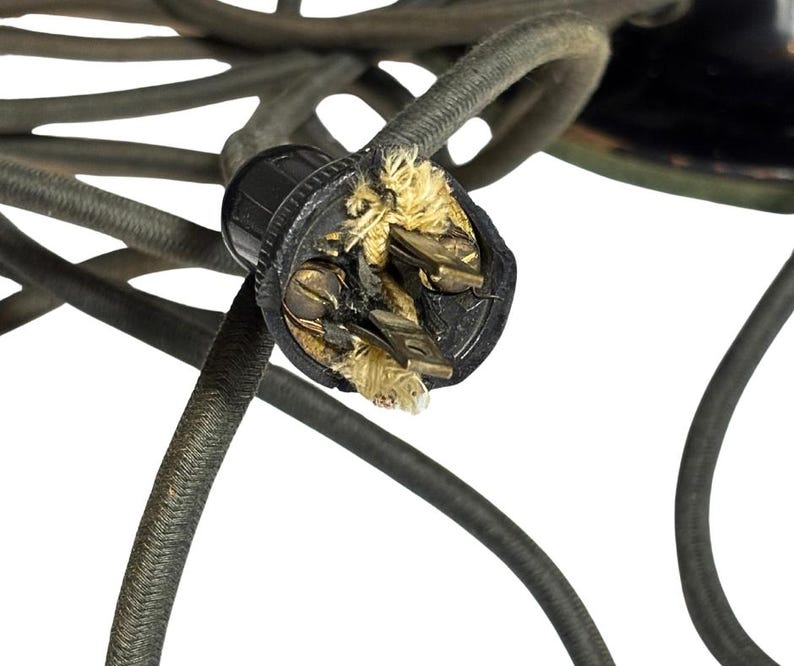 May include: Close-up of a damaged black electrical plug with exposed wires and frayed insulation. The plug is surrounded by several dark gray, braided electrical cords, suggesting a potential electrical hazard.