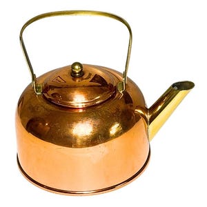 May include: A polished copper tea kettle featuring a rounded body, a matching lid with a small knob, a curved brass spout, and a thin, arched brass handle attached to the sides. The metal surface reflects light, showing a warm, metallic orange tone.