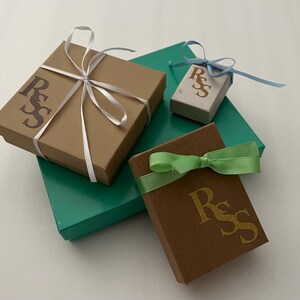 Puede incluir: Varias cajas de regalo en varios tama&ntilde;os y colores. Las cajas son marrones, turquesas y beige, con cintas a juego en blanco, azul claro y verde. Cada caja tiene las letras "RSS" impresas.