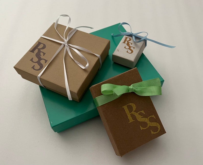 Puede incluir: Varias cajas de regalo en varios tama&ntilde;os y colores. Las cajas son marrones, turquesas y beige, con cintas a juego en blanco, azul claro y verde. Cada caja tiene las letras "RSS" impresas.