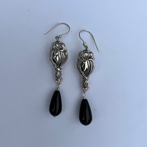 May include: Silver earrings with a detailed floral design and black teardrop-shaped stones.
