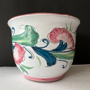 May include: White ceramic planter with a pink rim and hand-painted floral design in shades of green, blue, and pink.