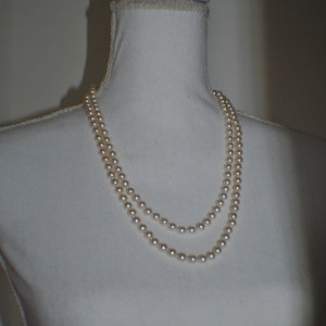 May include: A double strand of white pearl beads on a white mannequin.