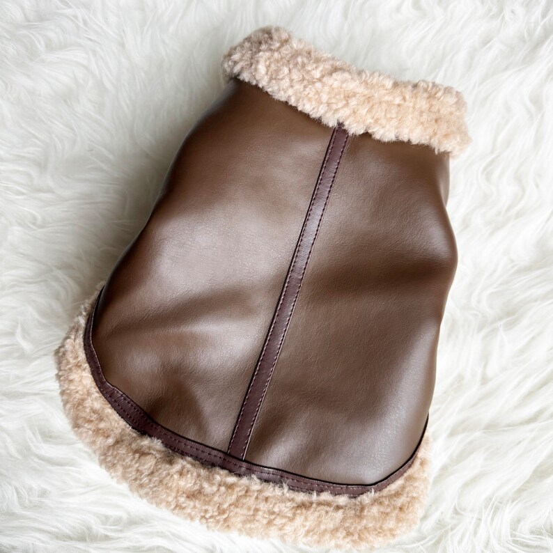 May include: A brown faux leather dog coat with a light brown faux fur trim.