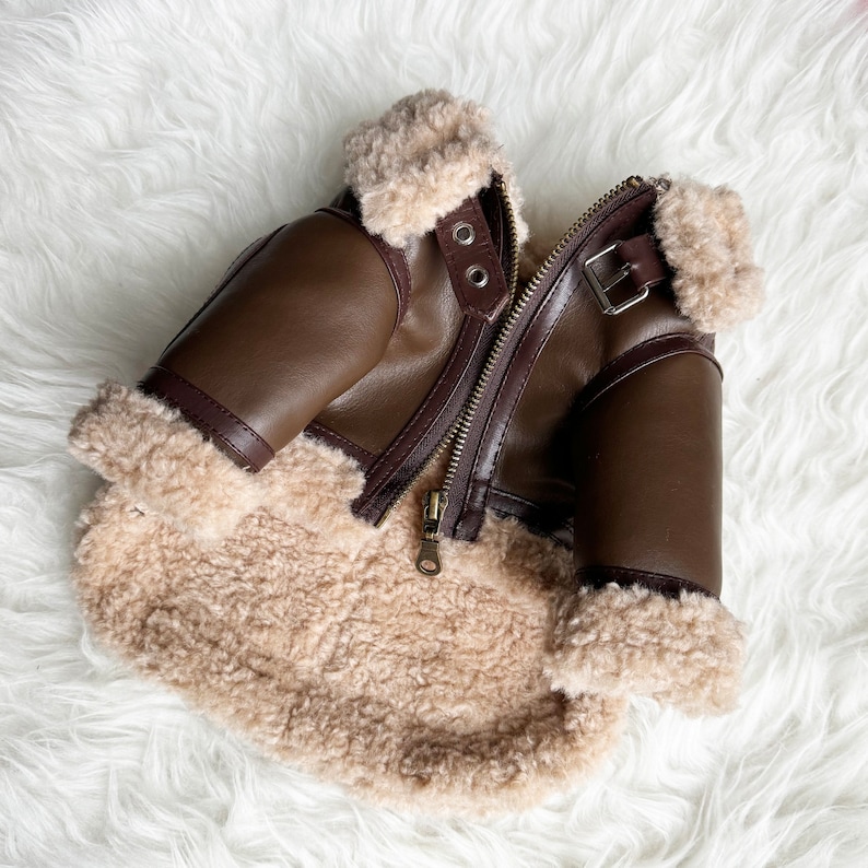 May include: A brown faux leather bomber jacket with a shearling lining. The jacket has a zipper closure and a buckle on the collar.