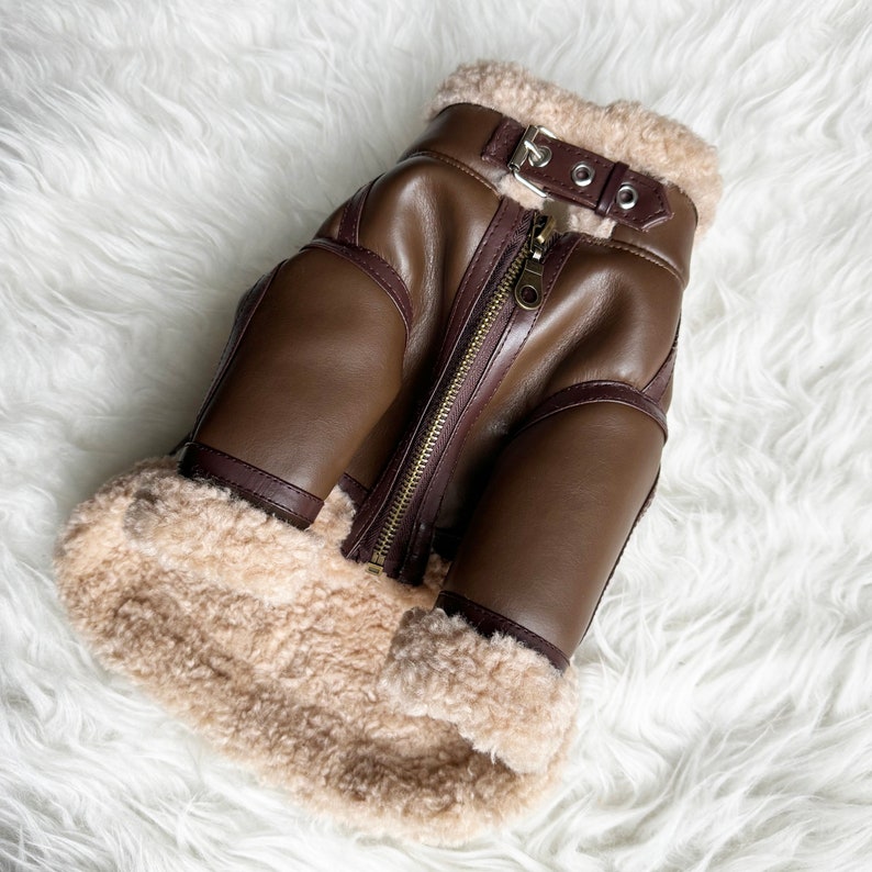 May include: A brown leather jacket with a shearling collar and zipper closure. The jacket has a brown leather trim and a zippered pocket on the left side.