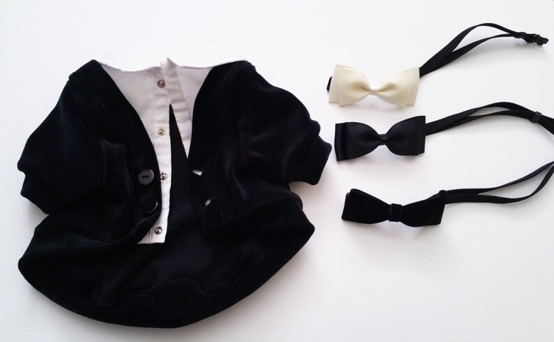 Pu&ograve; includere: Un completo per neonato in velluto nero con una camicia bianca abbottonata sotto. Sono inclusi tre papillon: uno bianco e due neri.